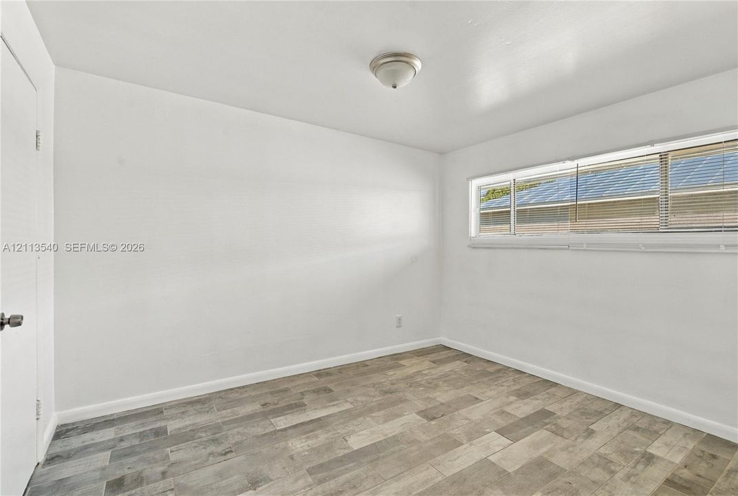 Neutral-toned room featuring wood-finish flooring, a horizontal sliding window, and a flush-mount ceiling light fixture