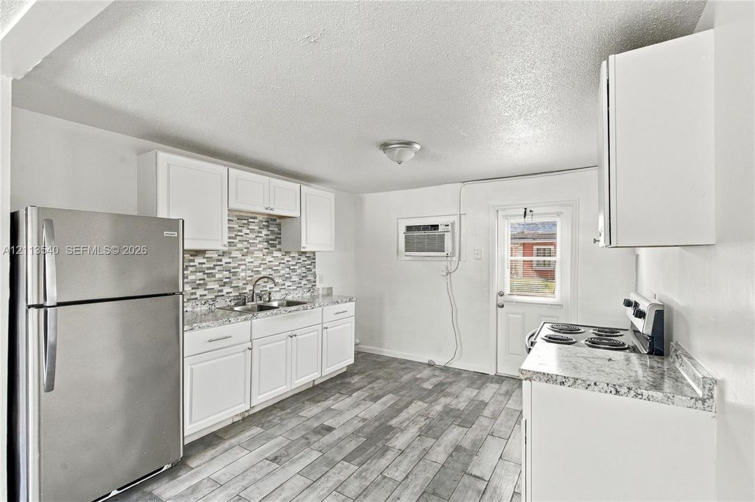 Kitchen featuring white cabinetry, stone-finish countertops, decorative multi-tone tile backsplash, stainless steel refrigerator, and wood-finish flooring