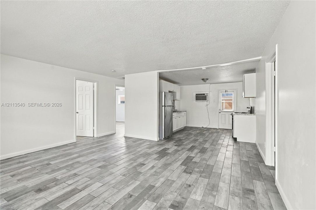 Open-concept interior featuring wood-finish flooring, stainless steel refrigerator, white cabinetry, and recessed lighting