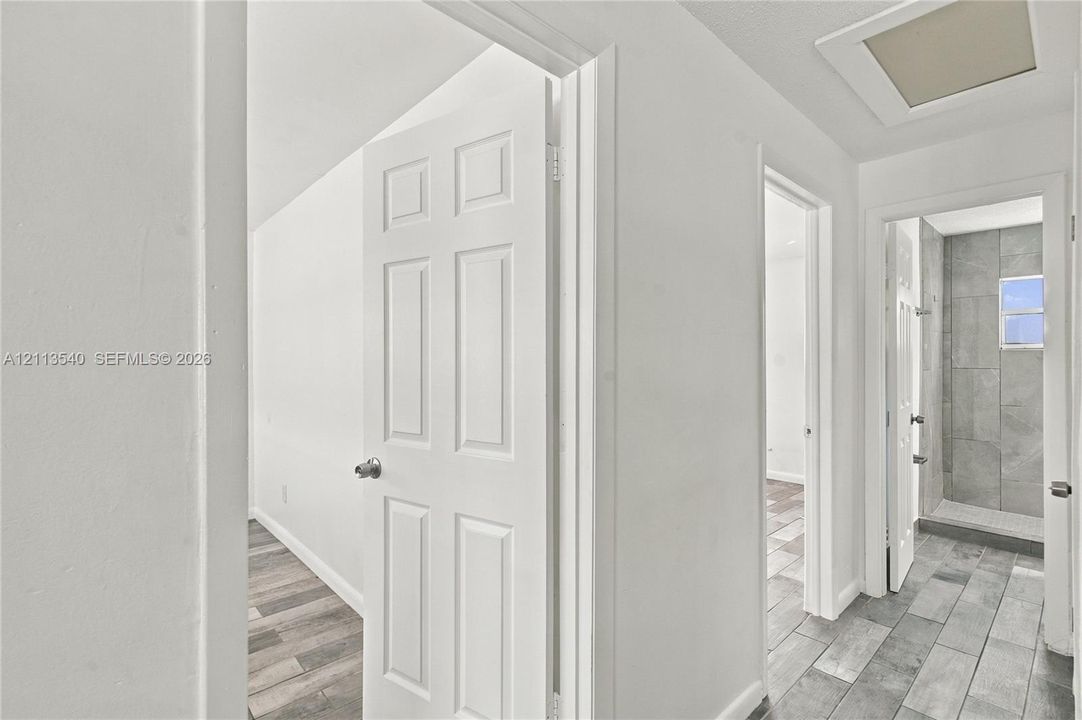Interior hallway featuring wood-finish flooring, white panel doors with metallic hardware, and a tiled shower stall with stone-finish wall cladding