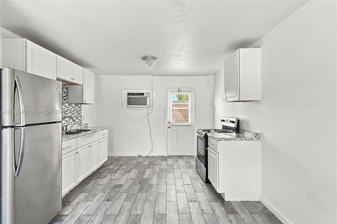 Kitchen featuring white cabinetry, stone-finish countertops, stainless steel appliances, mosaic tile backsplash, and wood-finish flooring