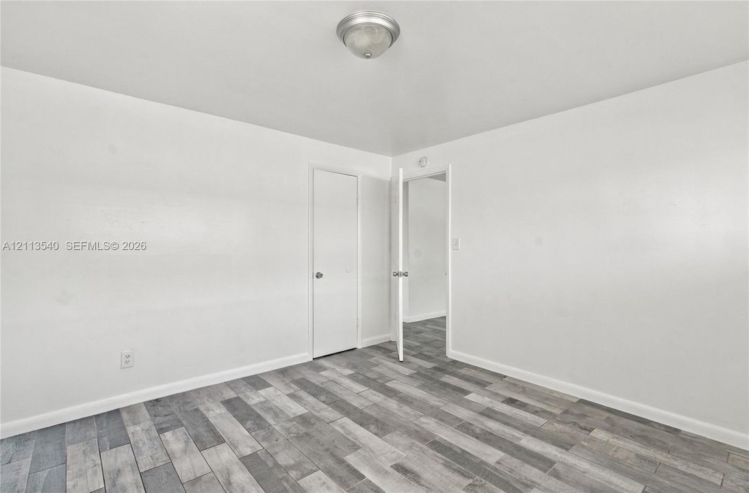 Neutral interior featuring wood-finish flooring, white walls, flush-mount ceiling lighting, and a single door entrance