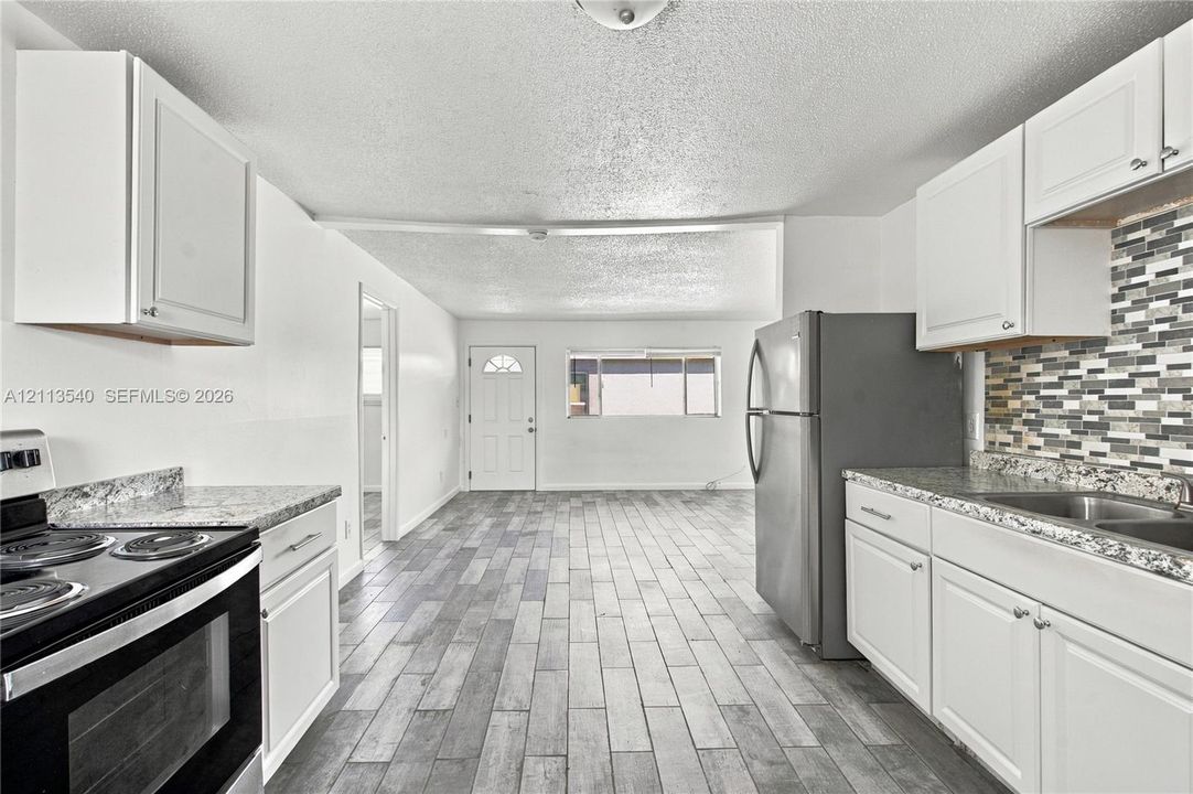 Kitchen featuring white cabinetry, stone-finish countertops, decorative tile backsplash, stainless steel appliances, and wood-finish flooring
