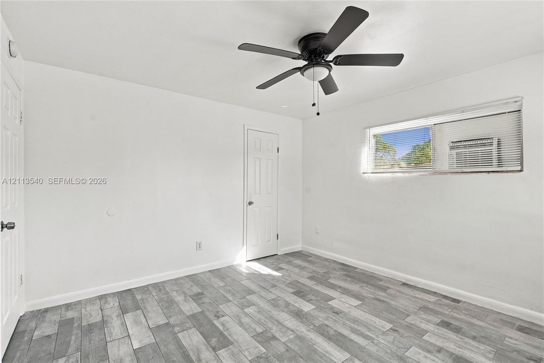Wood-finish flooring, multi-panel interior doors, and a ceiling-mounted fan with integrated lighting