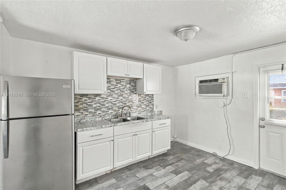 Kitchen featuring white shaker-style cabinetry, stone-finish countertops, mosaic tile backsplash, stainless steel refrigerator, and wood-finish tile flooring