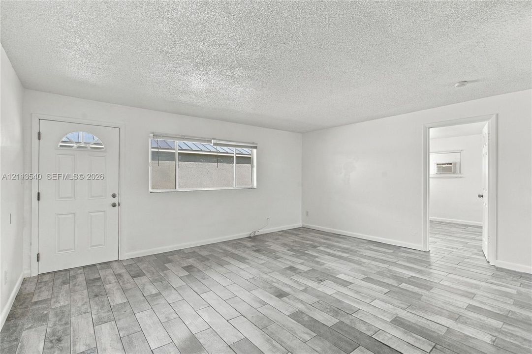 Interior space featuring wood-finish flooring, white walls, a multi-pane window, and an exterior entry door with a decorative glass insert
