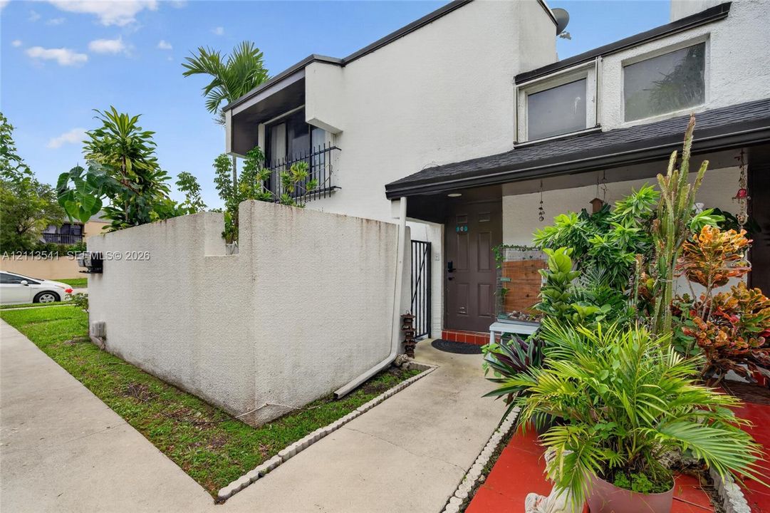 Stucco exterior featuring a private courtyard wall, second-story balcony with metal railing, and a covered entryway with red tiled threshold