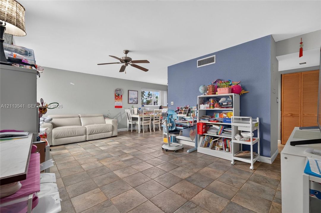 Open-concept interior featuring large-format tile flooring, a ceiling fan with integrated lighting, and louvered wood-finish closet doors