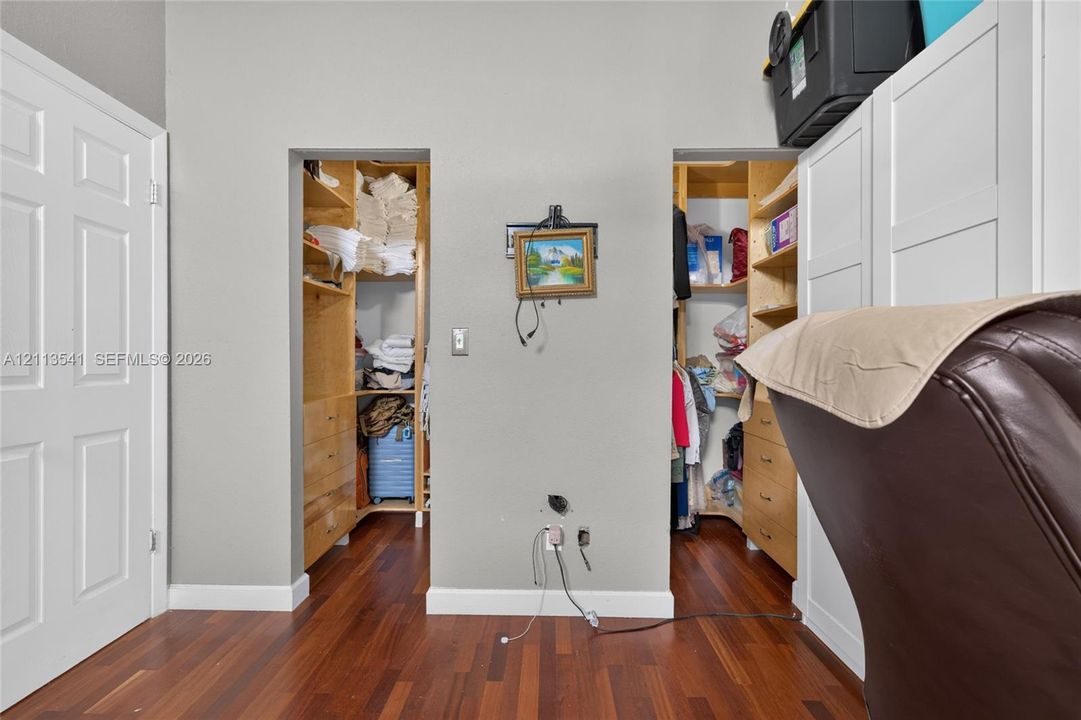 Wood-finish flooring, two walk-in storage areas with custom wood-finish built-in shelving, and white shaker-style cabinetry