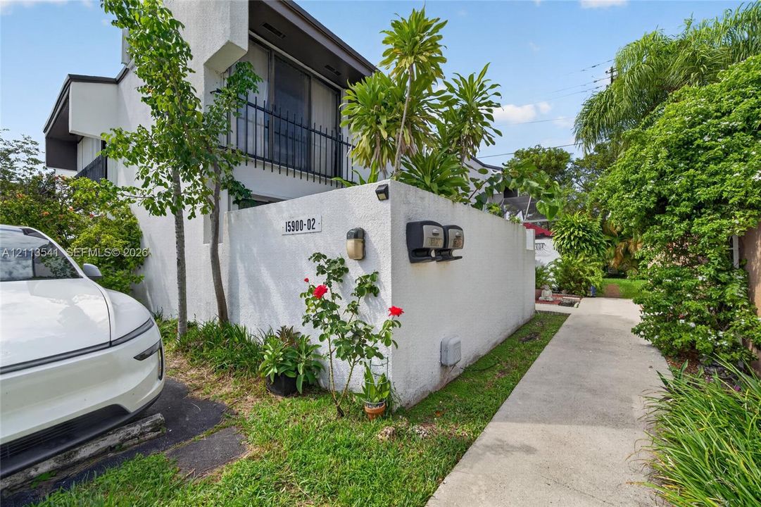 Stucco exterior featuring a walled courtyard, concrete walkway, wrought iron balcony railing, and mature landscaping