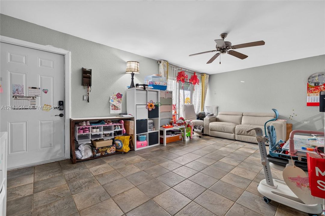 Living area featuring large-format ceramic tile flooring, a multi-blade ceiling fan, and sliding glass doors
