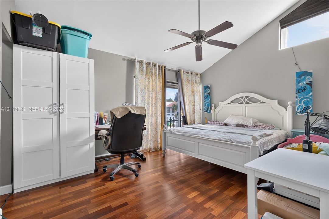 Vaulted ceilings featuring a central ceiling fan, wood-finish flooring, and a triangular clerestory window