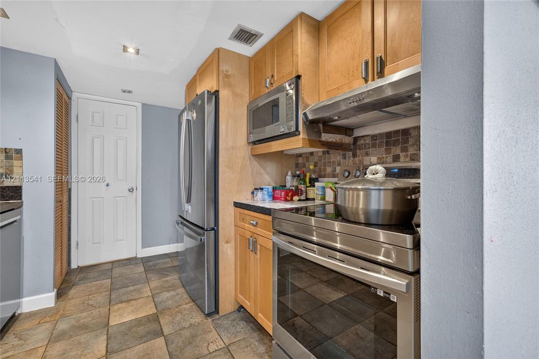 Kitchen featuring light-finish cabinetry, stainless steel appliances, stone tile backsplash, and stone-finish floor tiling