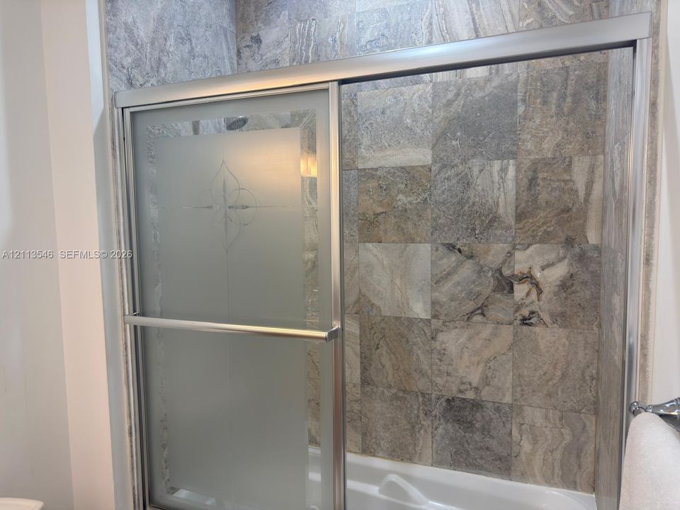 Shower enclosure featuring stone-tile wall surrounds, a sliding glass door with etched detailing, and a metallic frame