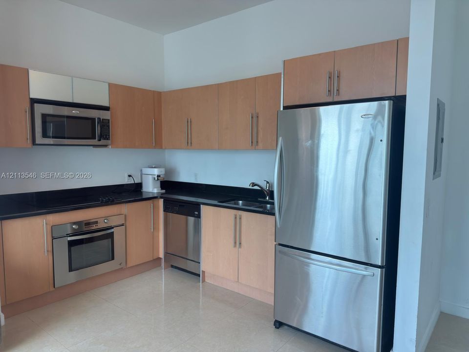 Kitchen featuring flat-panel wood-finish cabinetry, dark solid-surface countertops, stainless steel appliances, and tile flooring