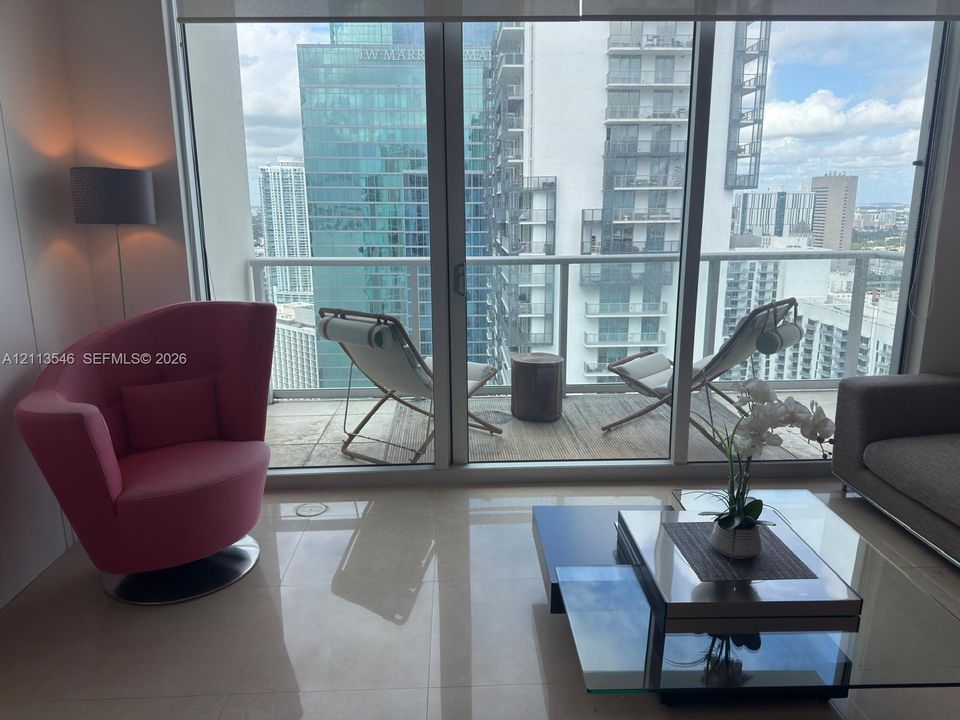 Floor-to-ceiling windows, private balcony with metal railing, and neutral tile flooring