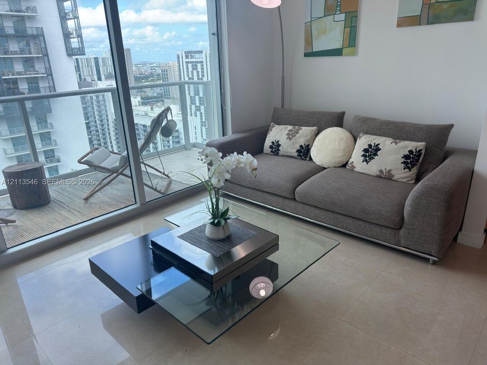 Floor-to-ceiling glass doors, neutral tile flooring, and a private balcony featuring a glass panel railing
