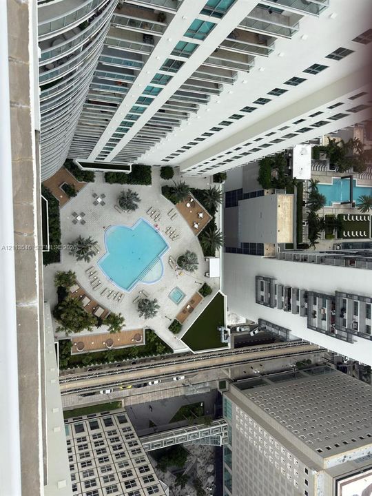 Aerial perspective of a high-rise exterior featuring a paved pool deck, custom-shaped swimming pool, built-in spa, and landscaped greenery