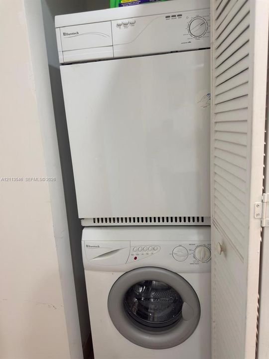 Stacked laundry center featuring a front-loading washer and louvered closet doors