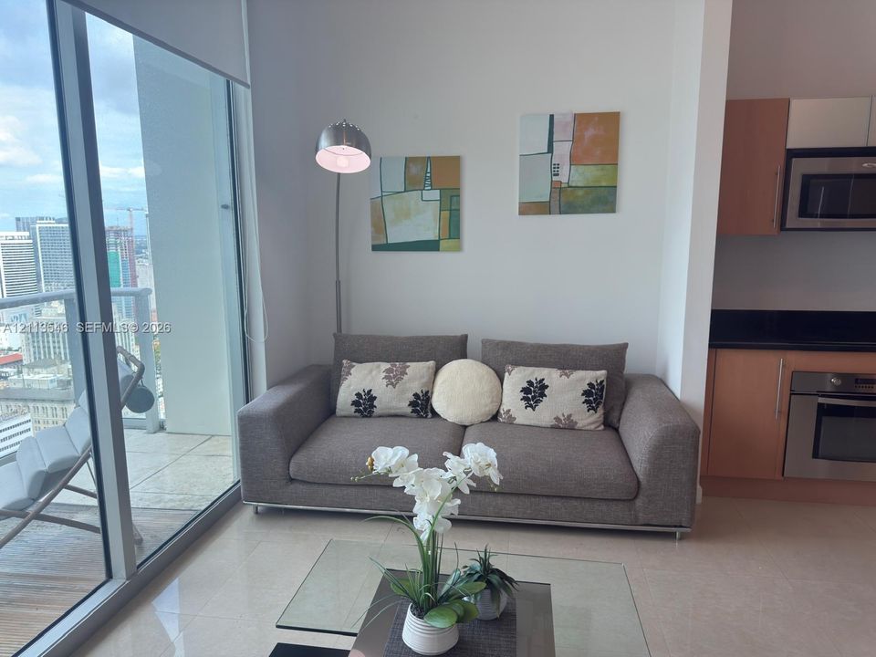 Floor-to-ceiling windows, light-toned tile flooring, and a kitchen featuring flat-panel cabinetry and stainless steel appliances