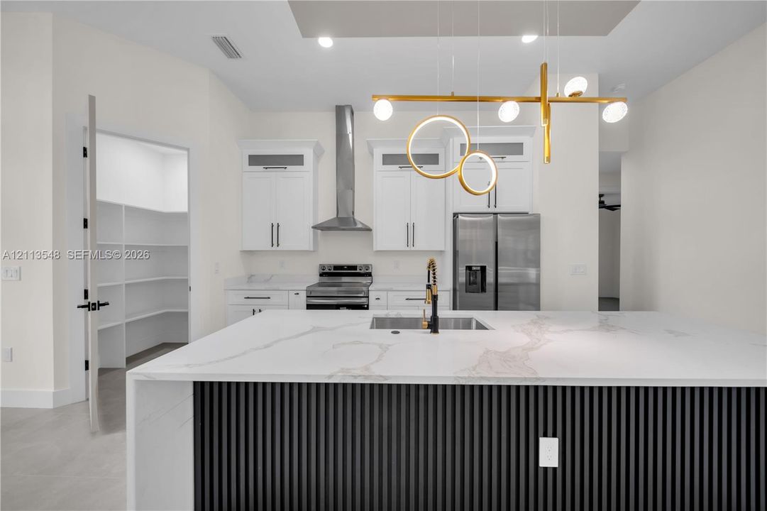 Kitchen island featuring a waterfall-edge stone countertop, decorative vertical-slatted base, and integrated sink with a gold-tone faucet