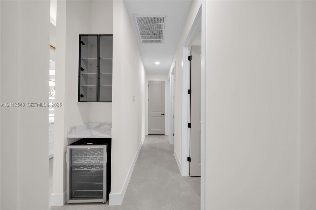 Built-in refreshment station featuring stone-composite countertop, glass-front cabinetry, and under-counter beverage cooler, complemented by neutral tile flooring and solid-core paneled doors