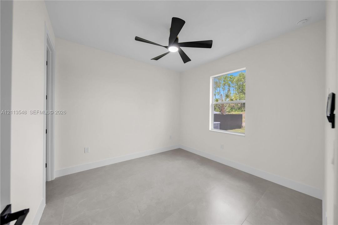 Neutral-toned interior featuring large-format tile flooring, a matte black five-blade ceiling fan with integrated lighting, and a single-pane window