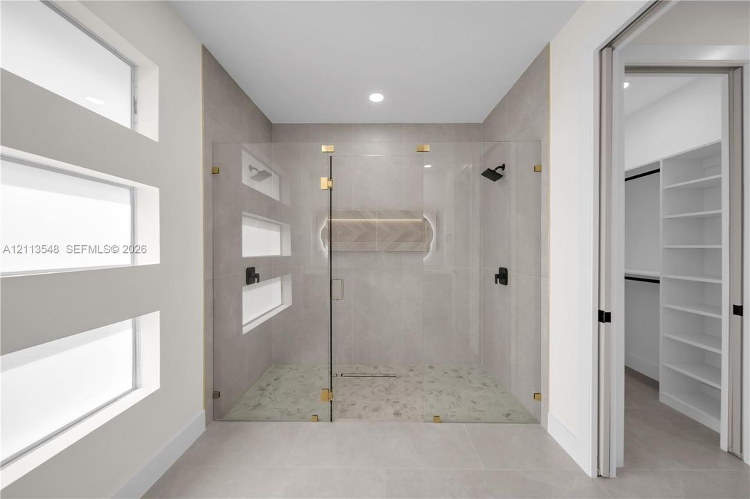 Walk-in shower featuring glass paneling, gold-tone hardware, recessed lighting, stone-tiled flooring, and a decorative herringbone inlay