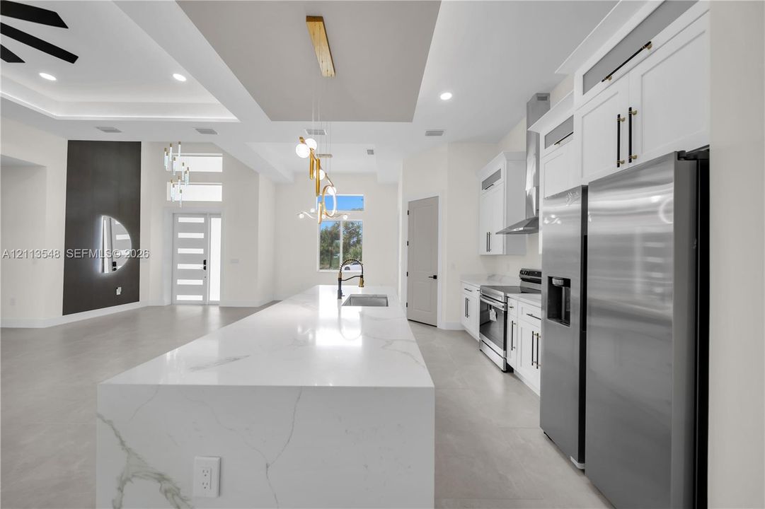 Kitchen featuring a large center island with a stone-finish waterfall countertop, stainless steel appliances, white cabinetry with matte black hardware, recessed ceiling lighting, and large-format tile flooring