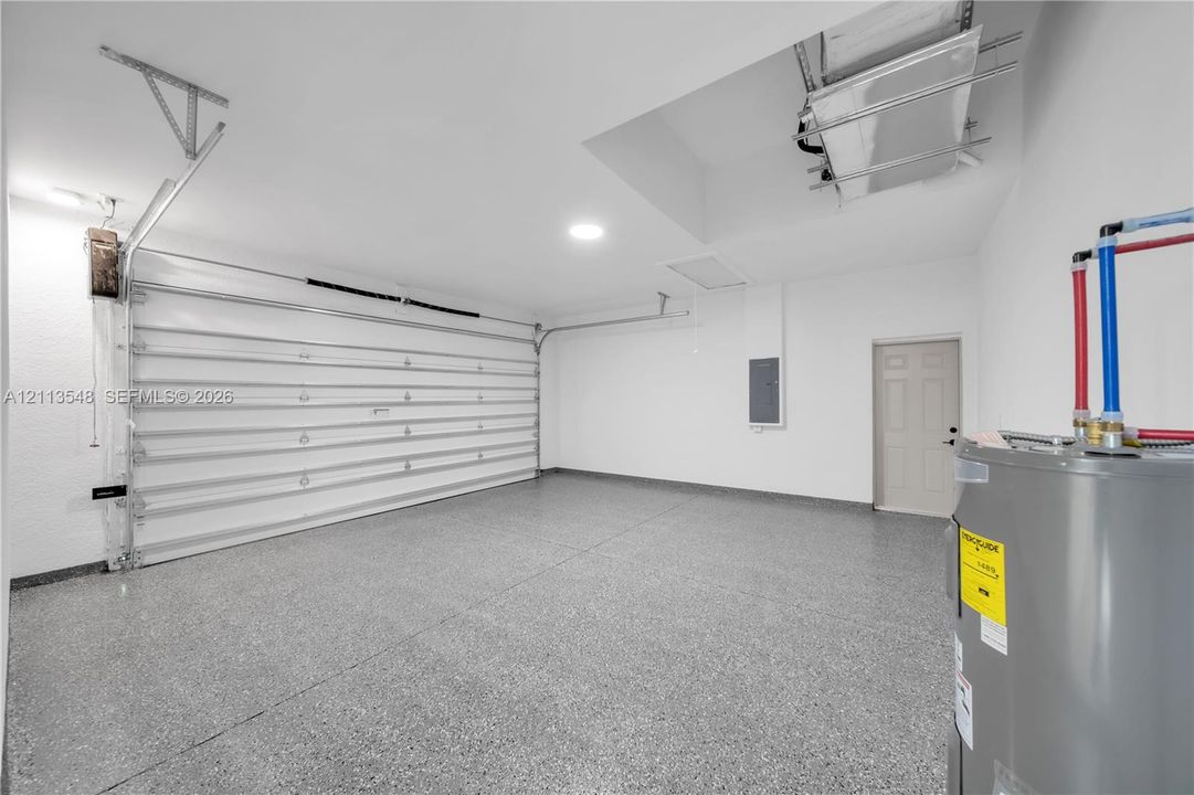 Garage featuring epoxy-coated flooring, insulated sectional garage door, recessed lighting, and water heater