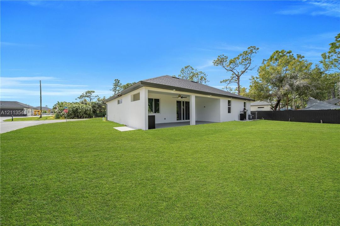 Exterior view featuring a concrete block construction with a hip roof, a covered patio with a ceiling fan, and an expansive lawn
