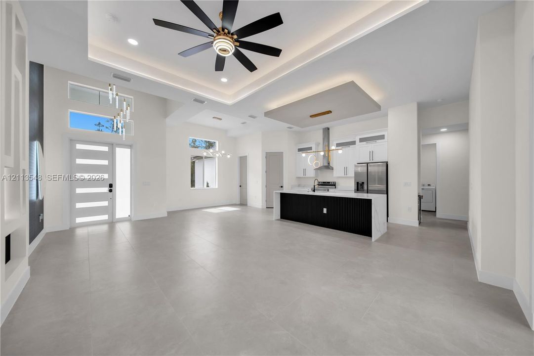 Open-concept interior featuring a coffered ceiling with recessed lighting, kitchen with a waterfall-edge island, tile flooring, and custom cabinetry