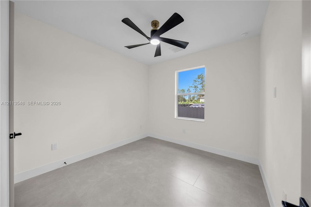 Neutral-toned room featuring large-format tile flooring, a multi-blade ceiling fan with integrated lighting, and a single-pane window