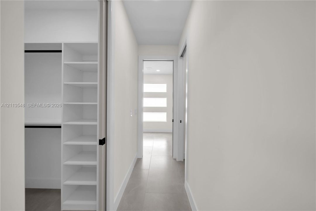 Walk-in closet featuring white built-in shelving, matte black hardware, and tile flooring