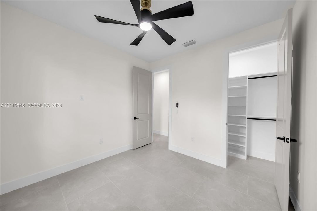 Neutral-toned tile flooring, contemporary multi-blade ceiling fan, and built-in closet shelving with hanging rods