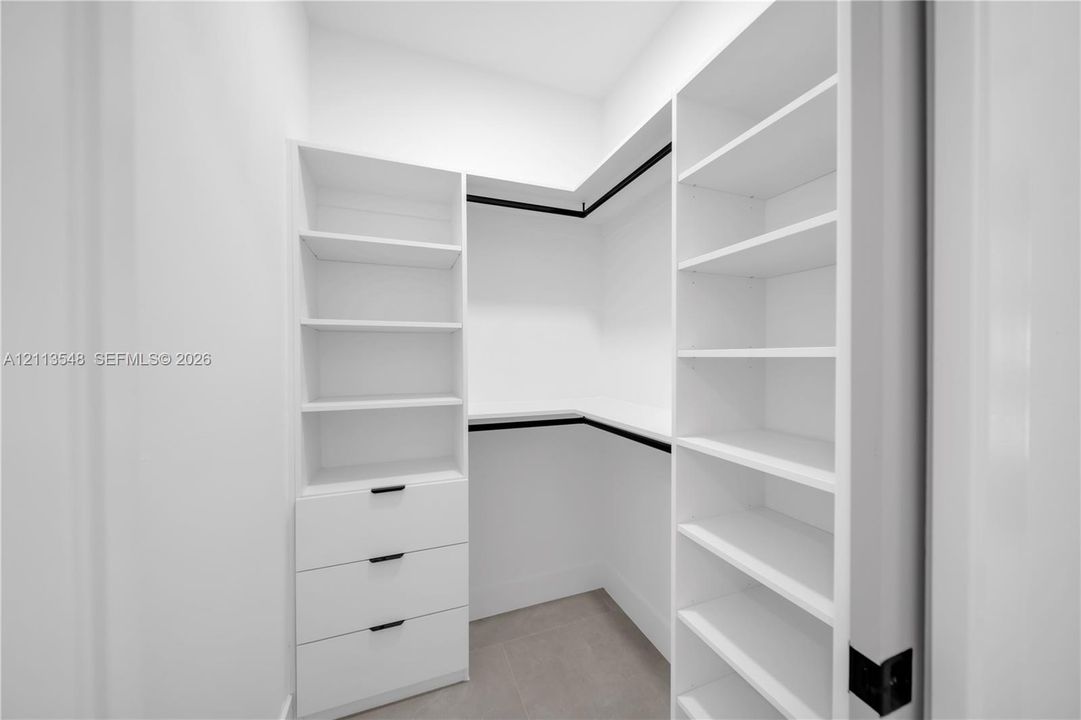 Custom walk-in closet featuring white built-in shelving, a three-drawer storage unit, matte black hardware, and hanging rods