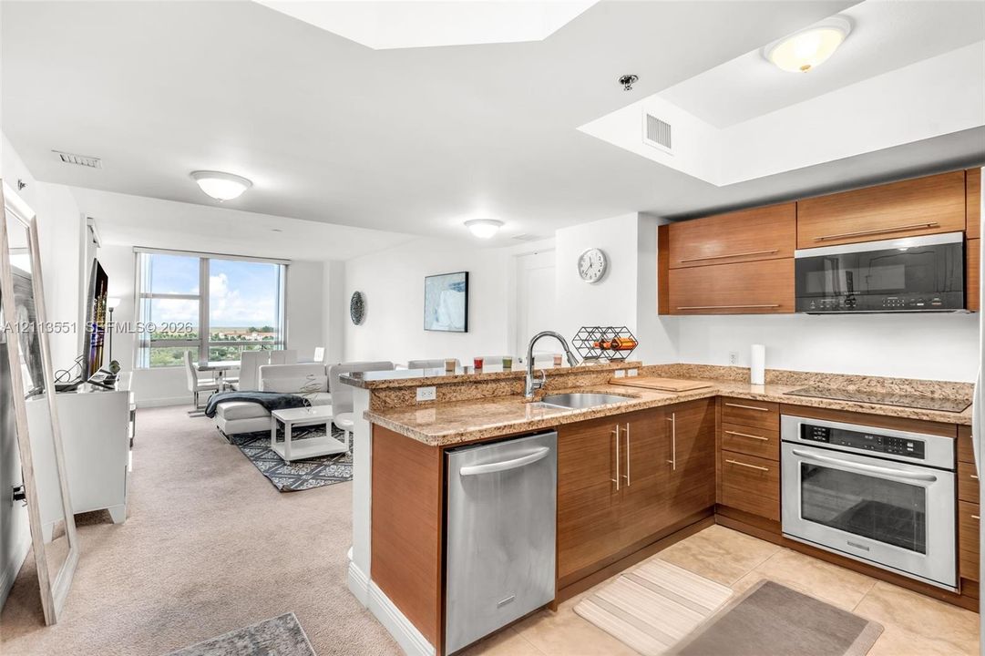 Kitchen featuring wood-finish cabinetry, stone countertops, stainless steel undermount sink, built-in oven, and stainless steel microwave