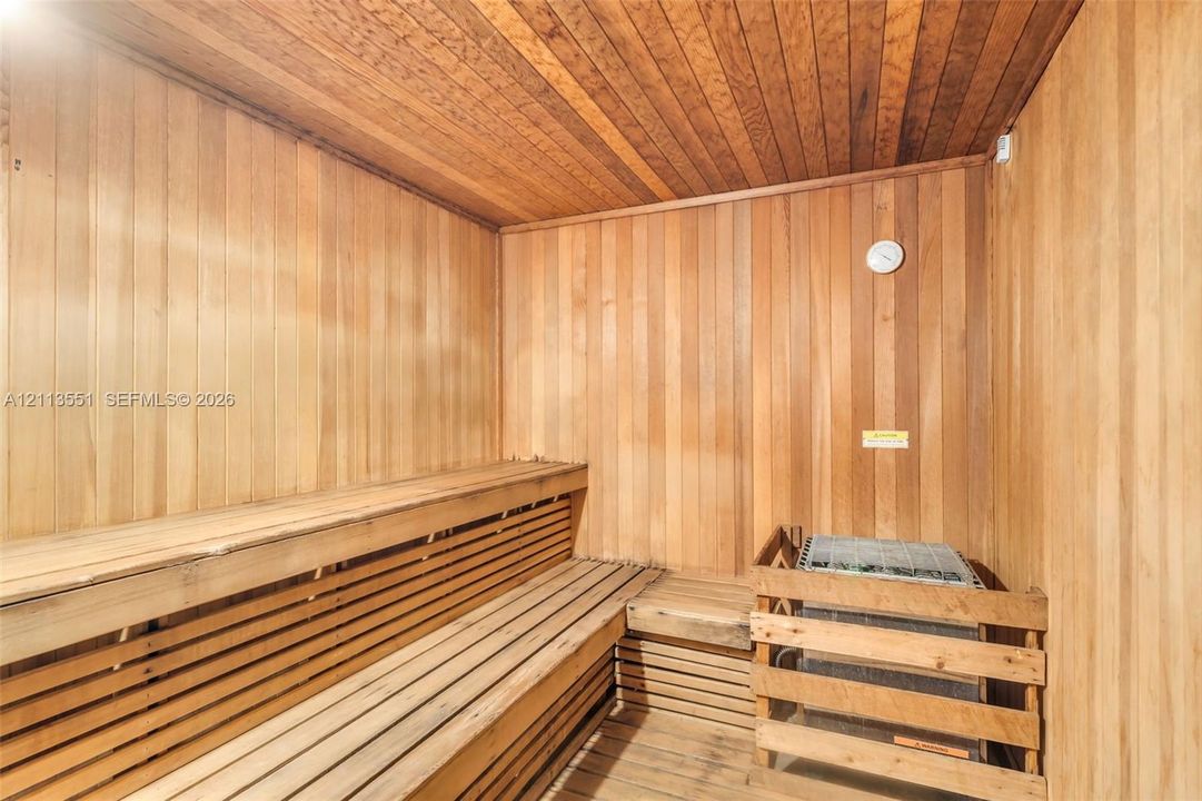 Sauna room featuring vertical wood-plank wall paneling, slatted wood bench seating, wood-finish ceiling, and a built-in protective heater guard