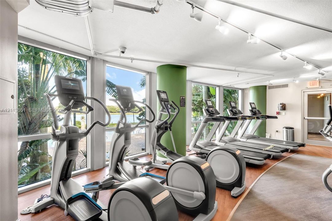 Fitness center featuring expansive floor-to-ceiling windows, wood-finish flooring, recessed track lighting, and structural columns