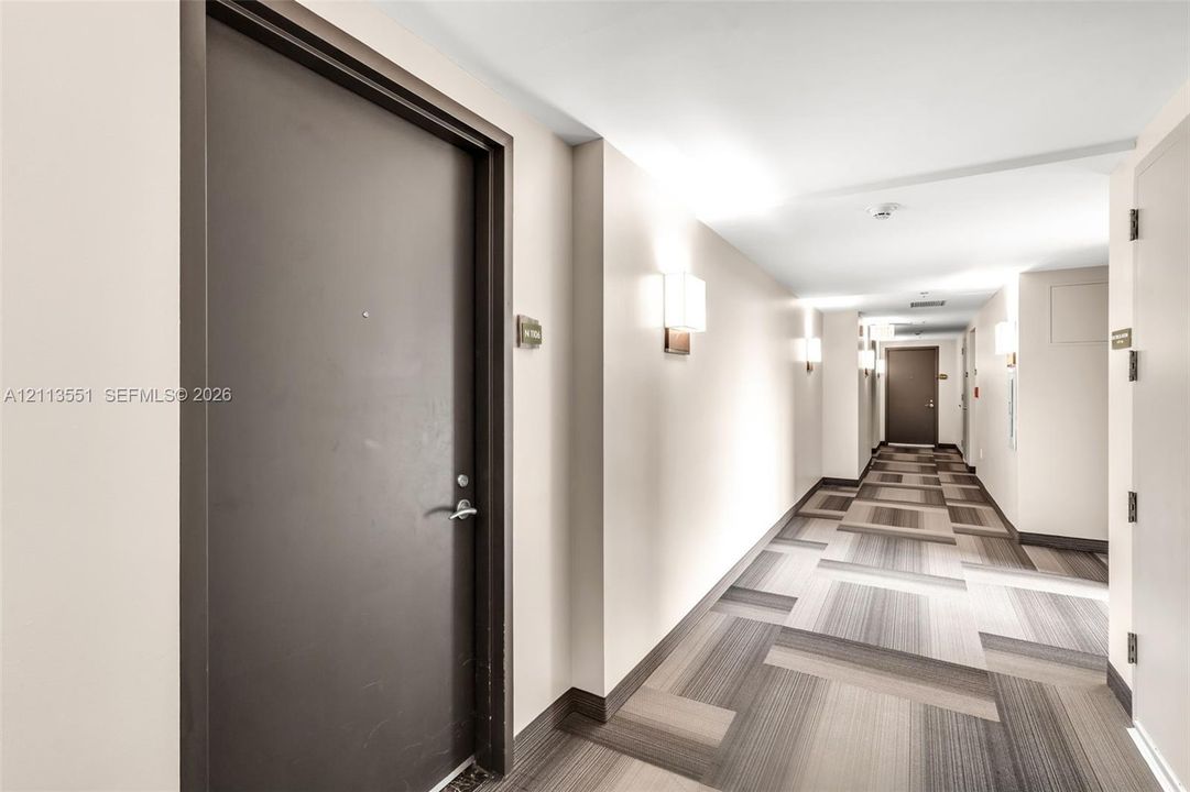 Interior corridor featuring neutral wall finishes, pattern-tiled flooring, and wall-mounted sconce lighting