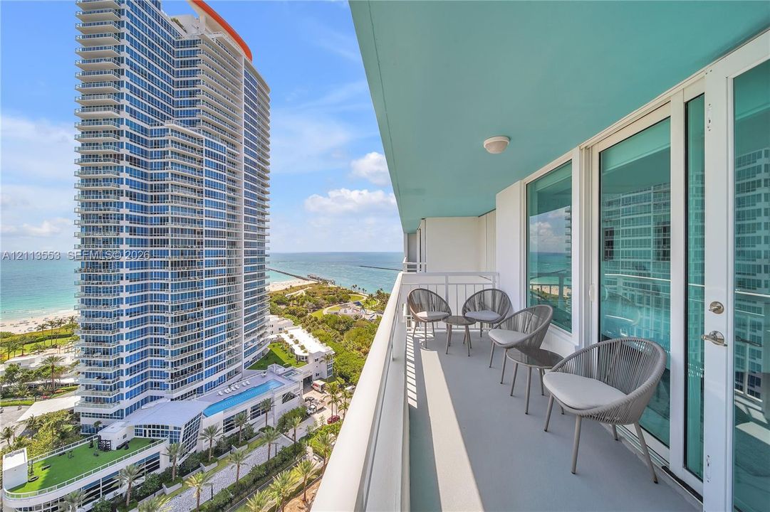 Covered balcony with a solid surface floor, white metal railing, and floor-to-ceiling glass sliding doors