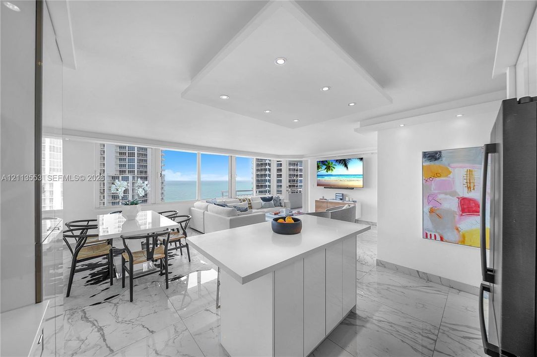 Open-concept space featuring expansive floor-to-ceiling windows, white cabinetry, a center island with a stone-finish countertop, and polished flooring with a marble-style pattern