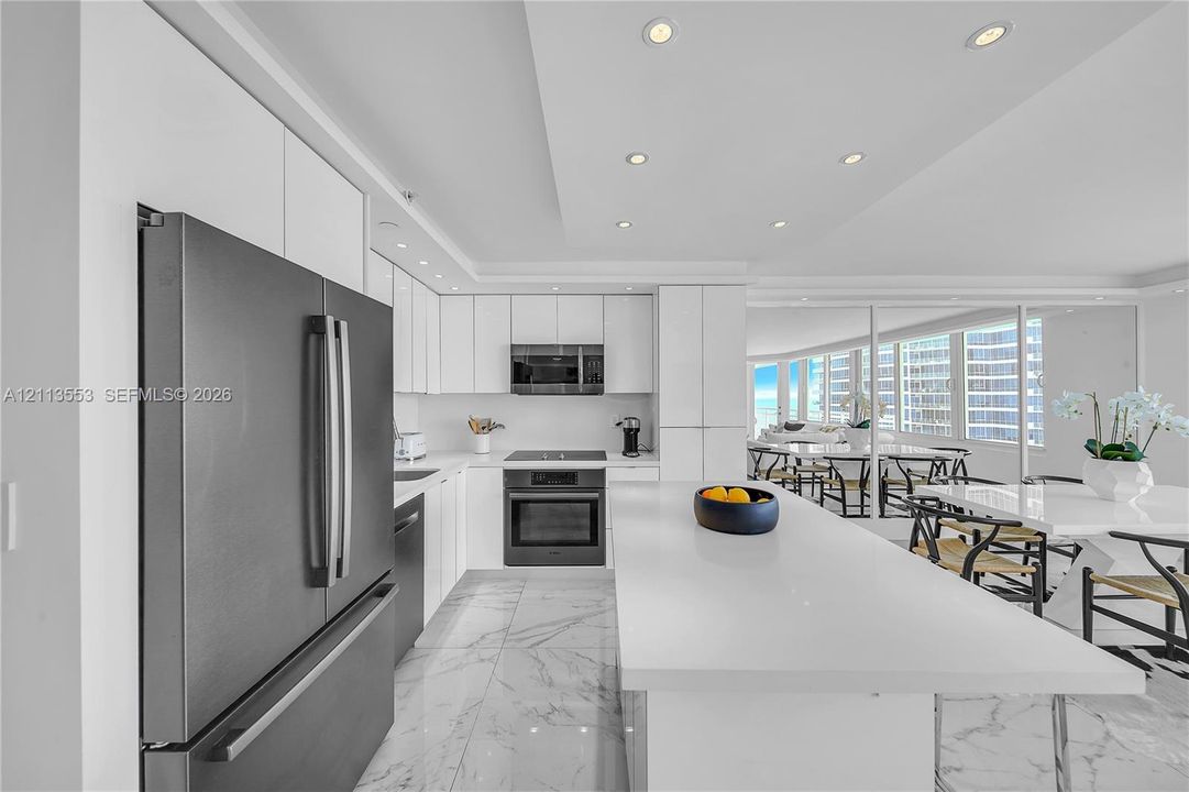 Kitchen featuring flat-panel white cabinetry, a center island with a stone-finish countertop, stone-finish flooring, recessed lighting, and stainless steel appliances