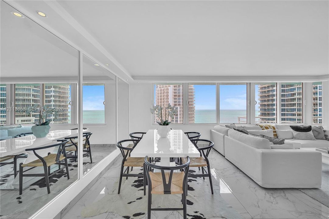 Open-concept living space featuring floor-to-ceiling windows, polished stone flooring, and expansive wall-mounted mirrors with integrated recessed lighting
