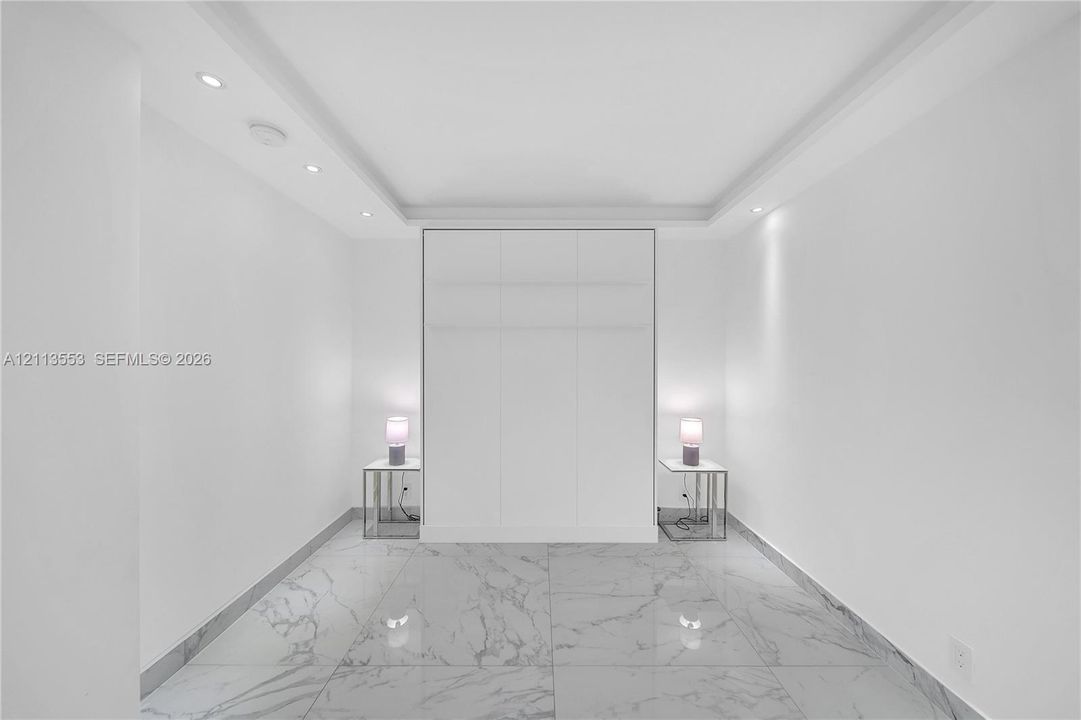 Large-format stone-look flooring, recessed ceiling lighting, tray ceiling architecture, and floor-to-ceiling built-in cabinetry
