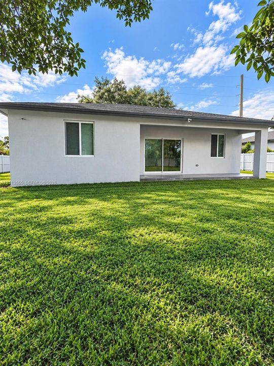 Rear exterior featuring a covered concrete patio, sliding glass doors, white vinyl perimeter fencing, and a manicured lawn