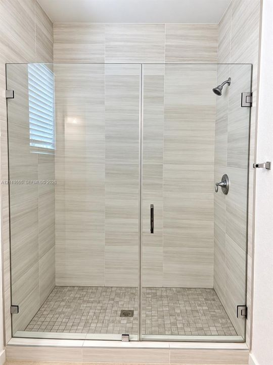 Walk-in shower featuring a frameless glass door, floor-to-ceiling large-format neutral tile, mosaic tile flooring, and wall-mounted metal fixtures