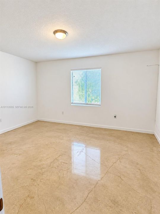 Neutral interior space featuring polished concrete flooring, white walls, and a single-light flush-mount ceiling fixture with an integrated window blind