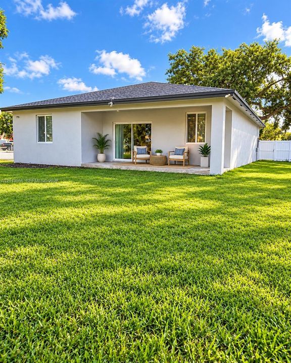 Exterior rear elevation featuring a covered concrete patio, sliding glass door, white vinyl fencing, and an expansive lawn