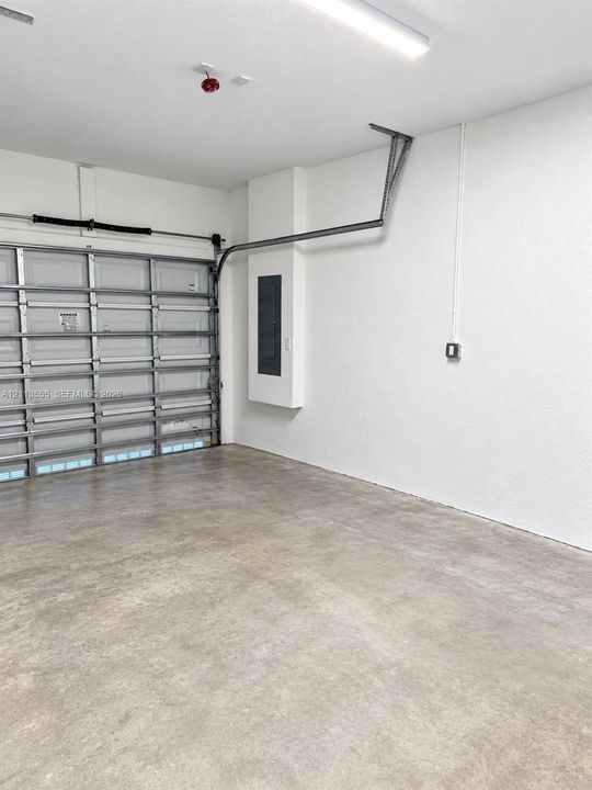Garage interior featuring a concrete floor, sectional overhead door, linear LED lighting, and a recessed electrical service panel